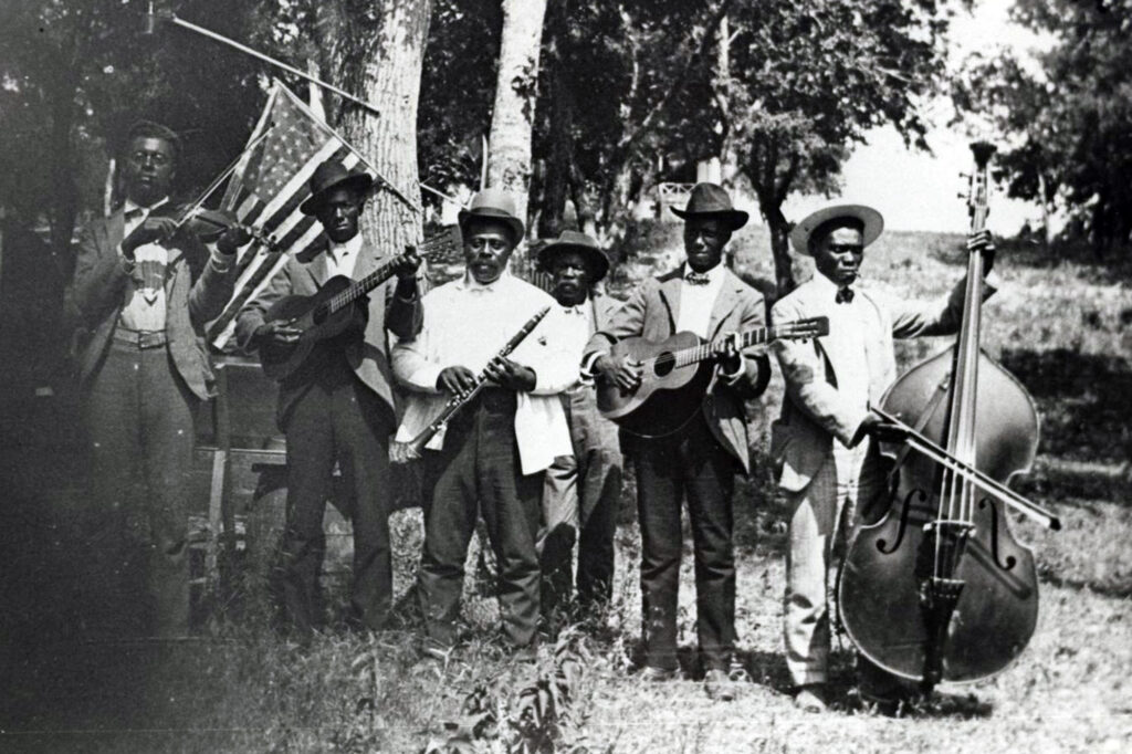 6 Black men dressed in suits standing in a field playing instruments